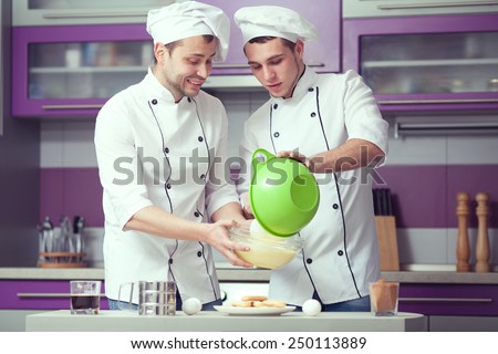 Tiramisu cooking concept. Portrait of two funny men in cook uniform making italian dessert in modern kitchen. Indoor shot