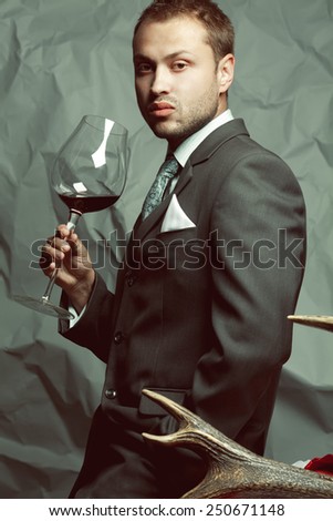 Red wine lover concept. Emotive portrait of handsome stylish man in elegant classic dark gray suit drinking wine. Baroque retro style. Studio shot