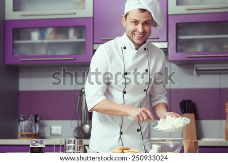 Tiramisu cooking concept. Portrait of smiling man in cook uniform making italian dessert in modern kitchen. Indoor shot