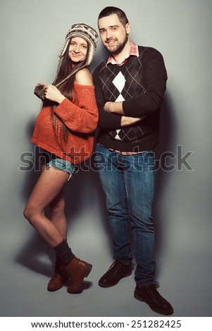 Stylish pregnancy and family concept: portrait of funny couple of hipsters (husband and wife) in trendy casual clothing smiling and posing over gray background. Urban street style. Studio shot