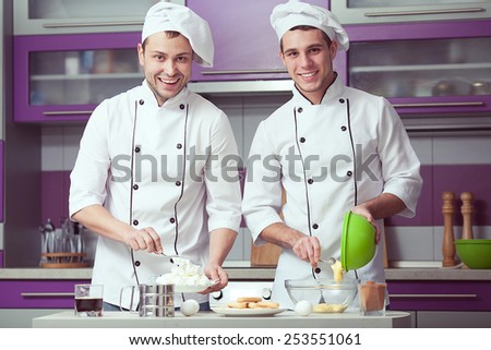 Tiramisu cooking concept. Portrait of two smiling men in cook uniform making italian dessert in modern kitchen. Indoor shot