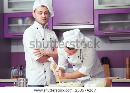 Tiramisu cooking concept. Portrait of two working men in cook uniform making italian dessert in modern kitchen. Indoor shot