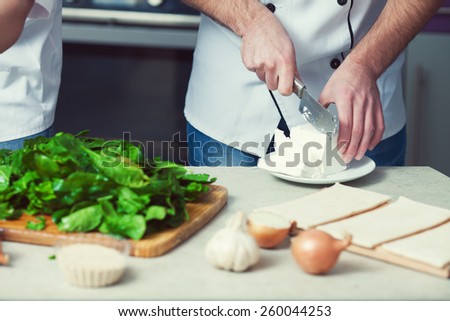 Vegetarian bakery concept. Chef\'s hands cutting feta cheese, spinach salad in kitchen of cafe, restaurant. Close up. Indoor shot