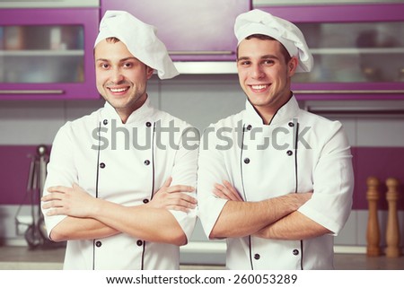 Portrait of two funny working men in cook uniform posing in modern kitchen. Indoor shot