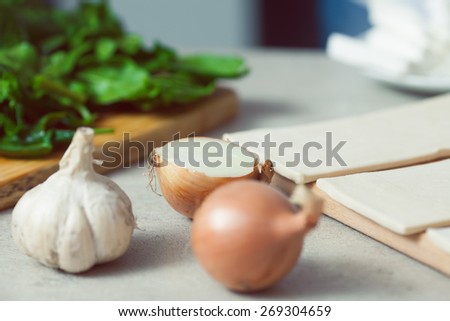 Vegetarian cooking concept. Spinach salad on wooden board, garlic, onion and pieces of dough in kitchen of cafe, restaurant. Close up. Indoor shot