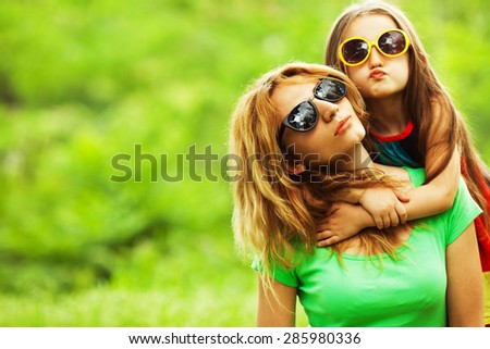 Happy family having fun. Baby girl with long brown hair and her mother with blond hair in trendy eyewear hugging each other. Close up. Copy-space. Outdoor shot