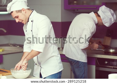 Cooking process concept. Portrait of two funny working men in cook uniform making food in modern kitchen. Indoor shot