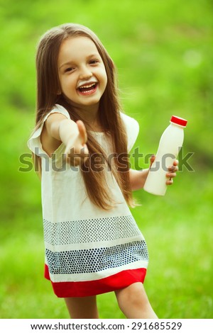 Milk products concept. Baby girl with long brown hair in white vintage summer dress drinking yogurt in the park, holding white plastic bottle, showing thumb up. Milk moustache under nose. Outdoor shot