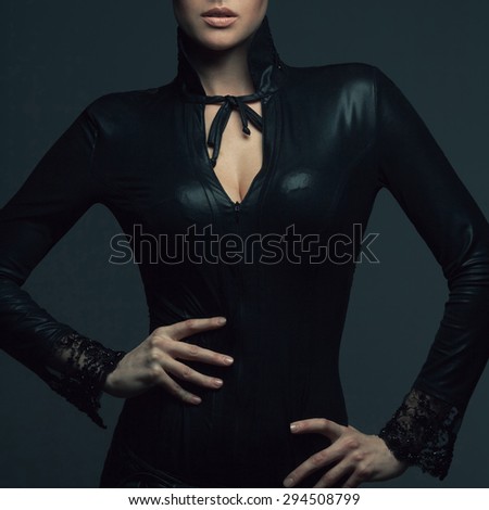 High fashion concept. Portrait of beautiful young woman in black leather dress with lace posing over dark gray background. Perfect natural make-up. Healthy skin. Close up. Studio shot