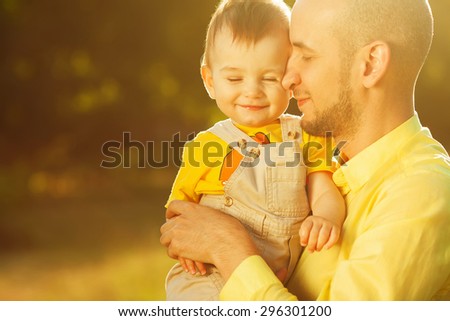 Happy family, friends forever concept. Smiling father and little son walking together in a park. Dad holding baby. Sunny summer day. Close up. Copy-space. Outdoor shot