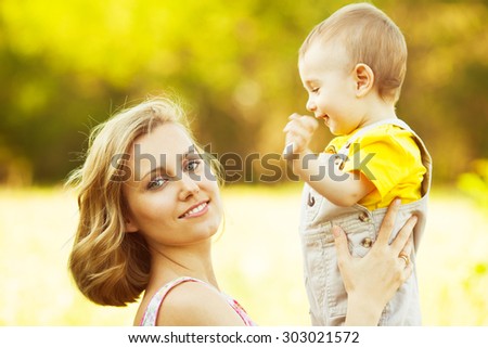 Happy family, friends forever concept. Smiling mother and little son playing together in a park. Mum holding smiling baby. Sunny windy summer day. Close up. Copy-space. Outdoor shot