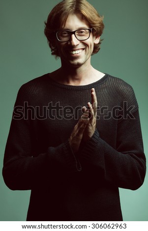 Stylish teacher, lecturer concept. Portrait of smiling young handsome man wearing fashion eyeglasses over orange background. Trendy black knitted sweater. Perfect long glossy hair. Studio shot