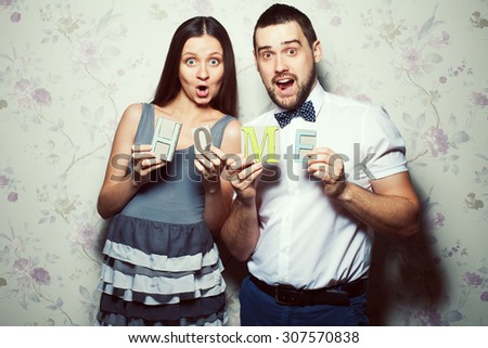 Home sweet home concept. Portrait of funny, happy couple of hipsters (husband and wife) in trendy clothes holding letters H O M E. Casual, vintage style. Studio shot