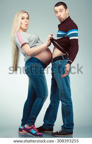 Funny sport training of future parents concept. Full length portrait of married couple touching bellies of each other, posing over gray background. Sporty style. Studio shot