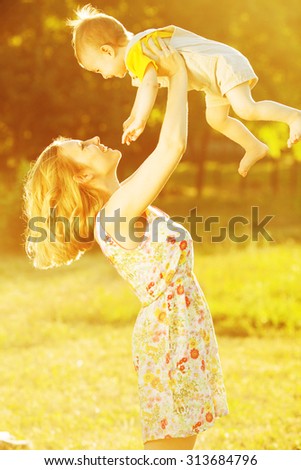 Happy family concept. Portrait of playing mother and little son in trendy summer clothing. Mommy tossing up toddler. Rays of light at summer sunrise. Outdoor shot
