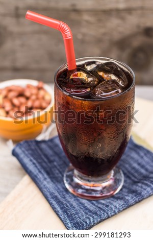 glass of cola with ice and salt roasted peanuts on wood table with copy-space