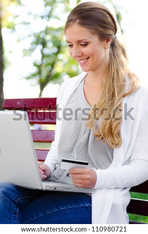 cheerful young woman with laptop and credit card sitting in a park