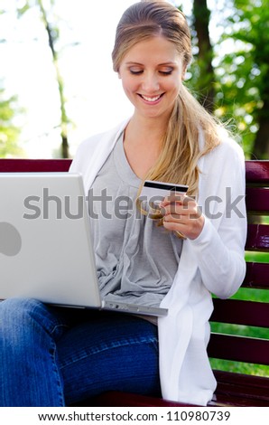 alluring woman sitting in a park with laptop and holding credit card