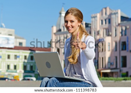 successful student sitting with laptop and showing thumbs up in street