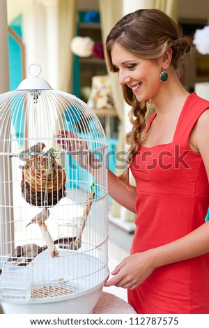 attractive young woman looking at birds in white cage and smiling
