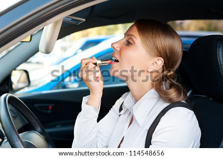 attractive young woman sitting in the car and painting her lips