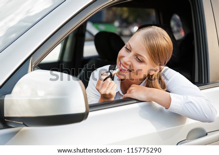 alluring woman sitting in the car, looking at mirror and painting her lips