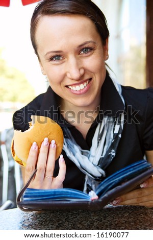 woman with burger reading book in cafe