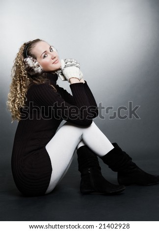 smiley woman in mitten and furs headphones sitting in studio over dark background