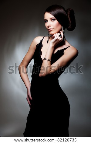 alluring woman in black dress posing over dark background