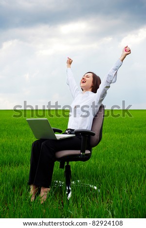 happy businesswoman with computer sitting on chair over green field
