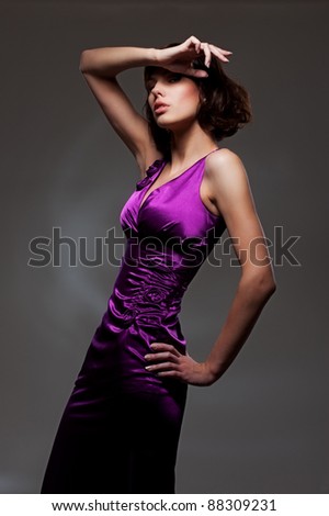 alluring woman in evening violet dress posing over dark background