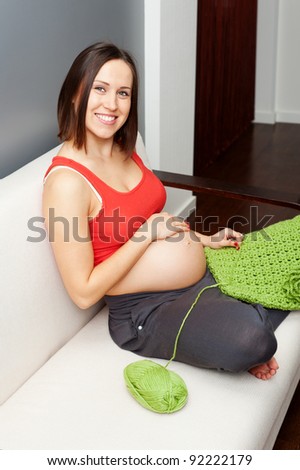 smiley pregnant woman sitting on sofa and crocheting