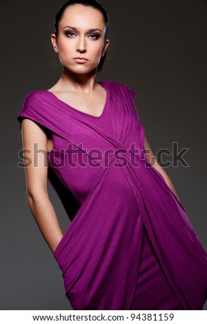 alluring woman in violet dress posing over dark background