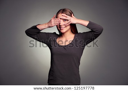 smiley young woman peeping through her fingers. studio shot over dark background