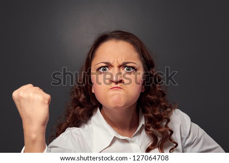 angry young woman threatening the fist over grey background