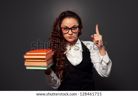 young teacher in glasses with pile of books make attention sign. picture over dark background