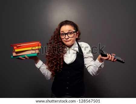 funny woman in glasses with pile of books and tv remote. picture over dark background