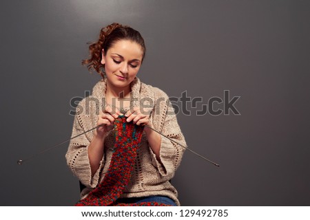 smiley girl holding needles and knitting scarf. studio shot over dark background
