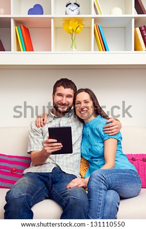 smiley couple sitting on sofa and holding the tablet pc