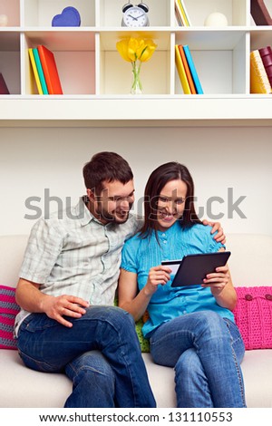 smiley couple sitting on sofa and shopping on the internet