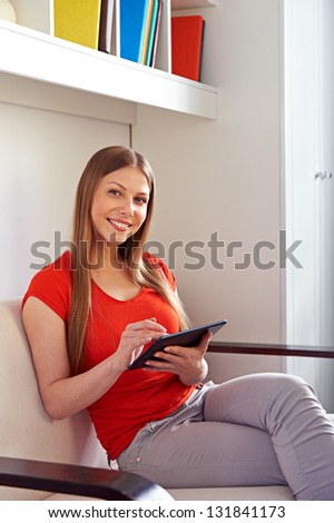 smiley beautiful woman in orange t-shirt working with tablet pc at home