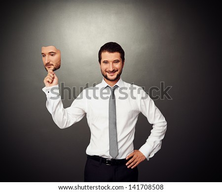smiley businessman holding serious mask over dark background