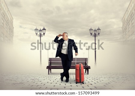 senior man standing on the square holding suitcase and looking forward