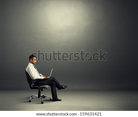 concentrated young businessman sitting in empty dark room and working with laptop