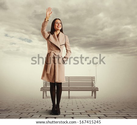 happy young woman standing against bench and waving hand