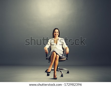 smiley young businesswoman sitting on the office chair over dark background