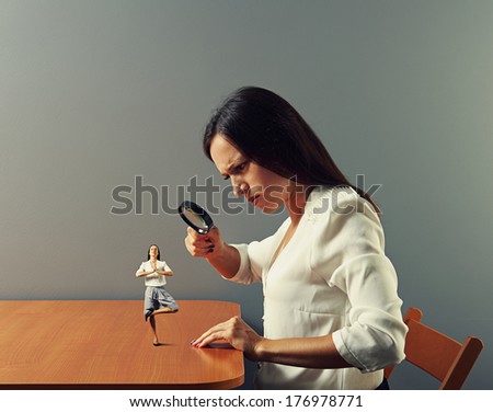 serious businesswoman looking with magnifying glass at small meditation woman