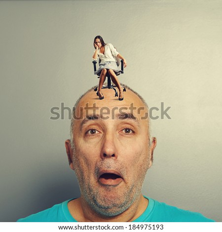 amazed man with small tired woman on his head over grey background