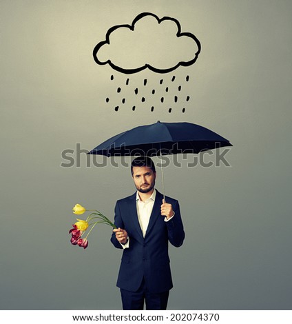 sad young man with black umbrella and drooped flowers standing under drawing storm cloud. photo over grey background