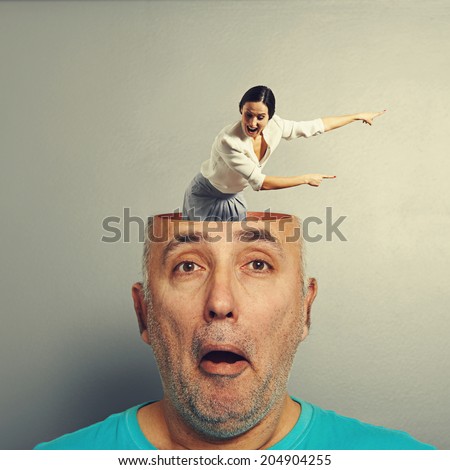 amazed senior man with open head. young screaming businesswoman standing in the head, looking at the man and pointing at something. photo over grey background